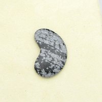 Snowflake obsidian cabochon is kidney-shaped opaque black stone with gray blotches. Smoothly polished gemstone measures 40mm long, 22mm wide, and 4mm thick, with a weight of approximately 33.80 carats.
