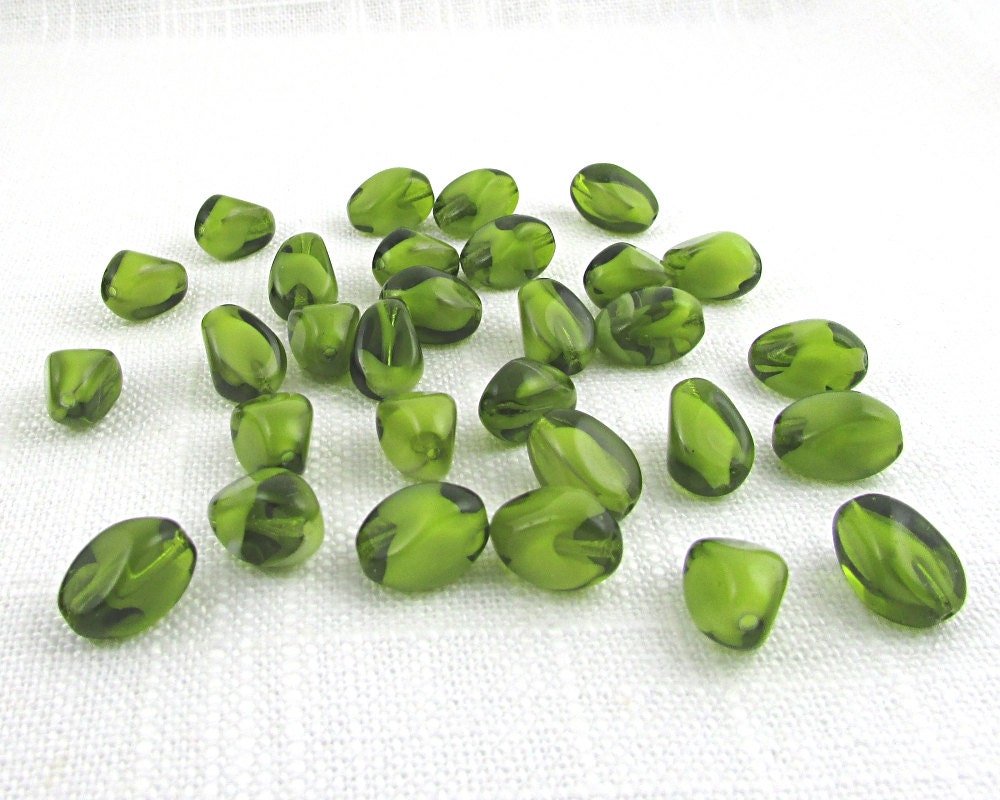 Olivine Czech glass givre beads are twisted ovals of translucent green pressed glass with opaque white inclusions. Beads measure approximately 13mm long and 9mm diameter, with 1mm lengthwise holes.