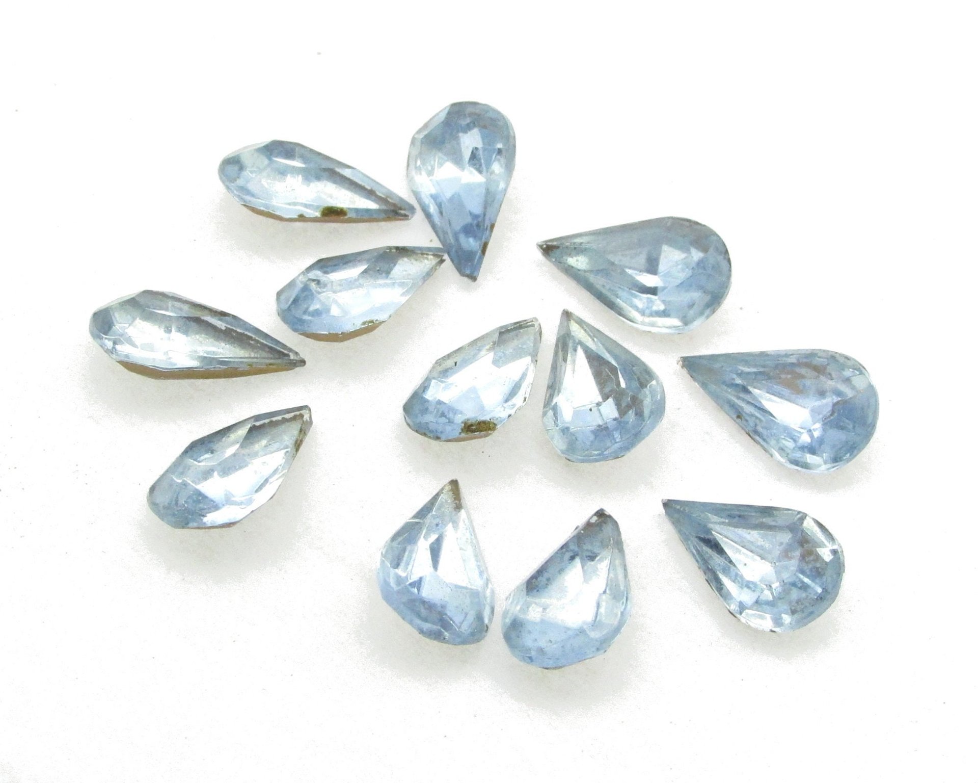 Vintage tin table cut pear shape rhinestones are translucent light sapphire blue backed with gold foil. Point back stones measure 13mm long and 7.8mm wide.