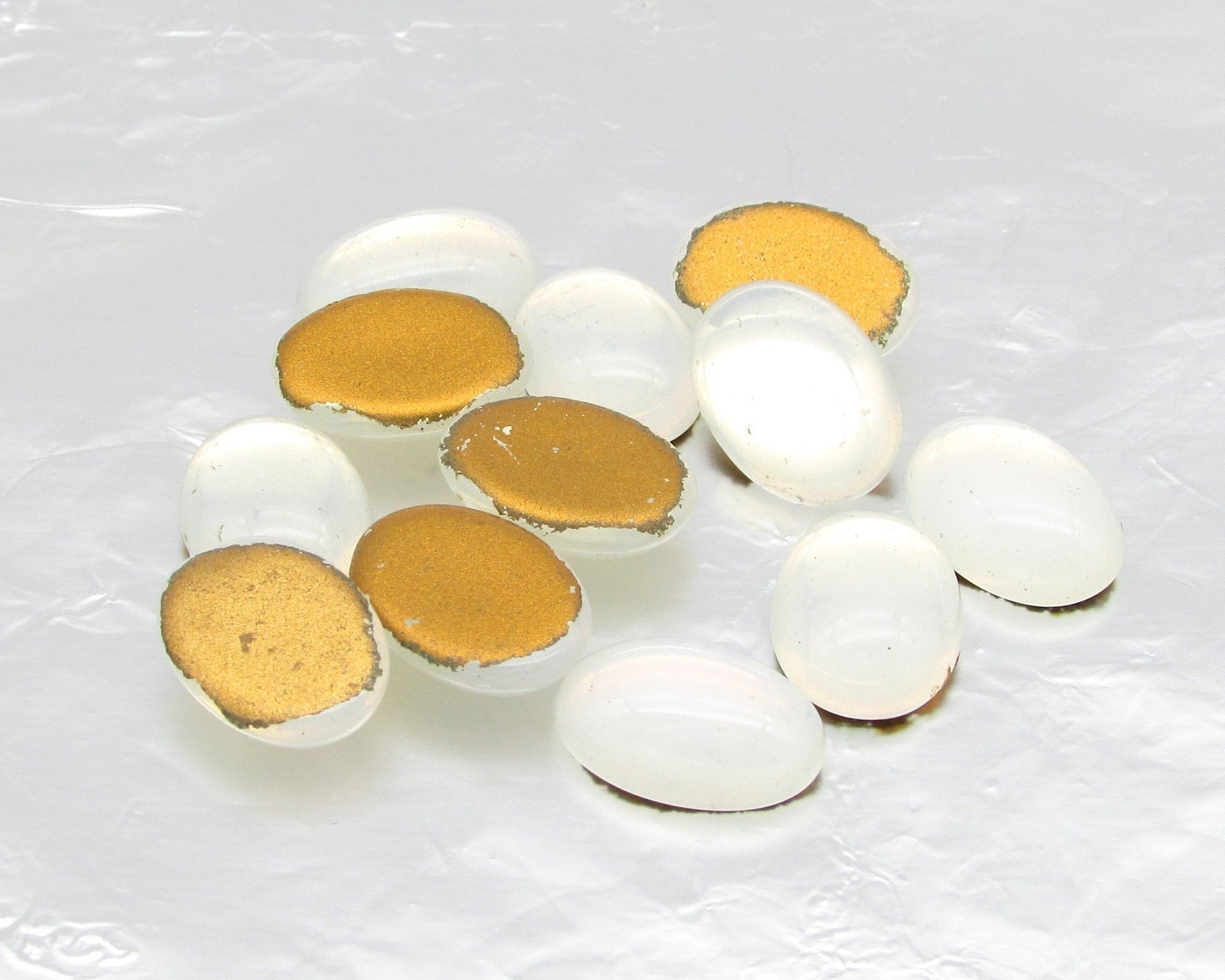 Vintage glass cabochons are semi-translucent opaline white with gold foil. Flat back gems measure 14mm long by 10mm wide, with a smooth 5mm dome. 