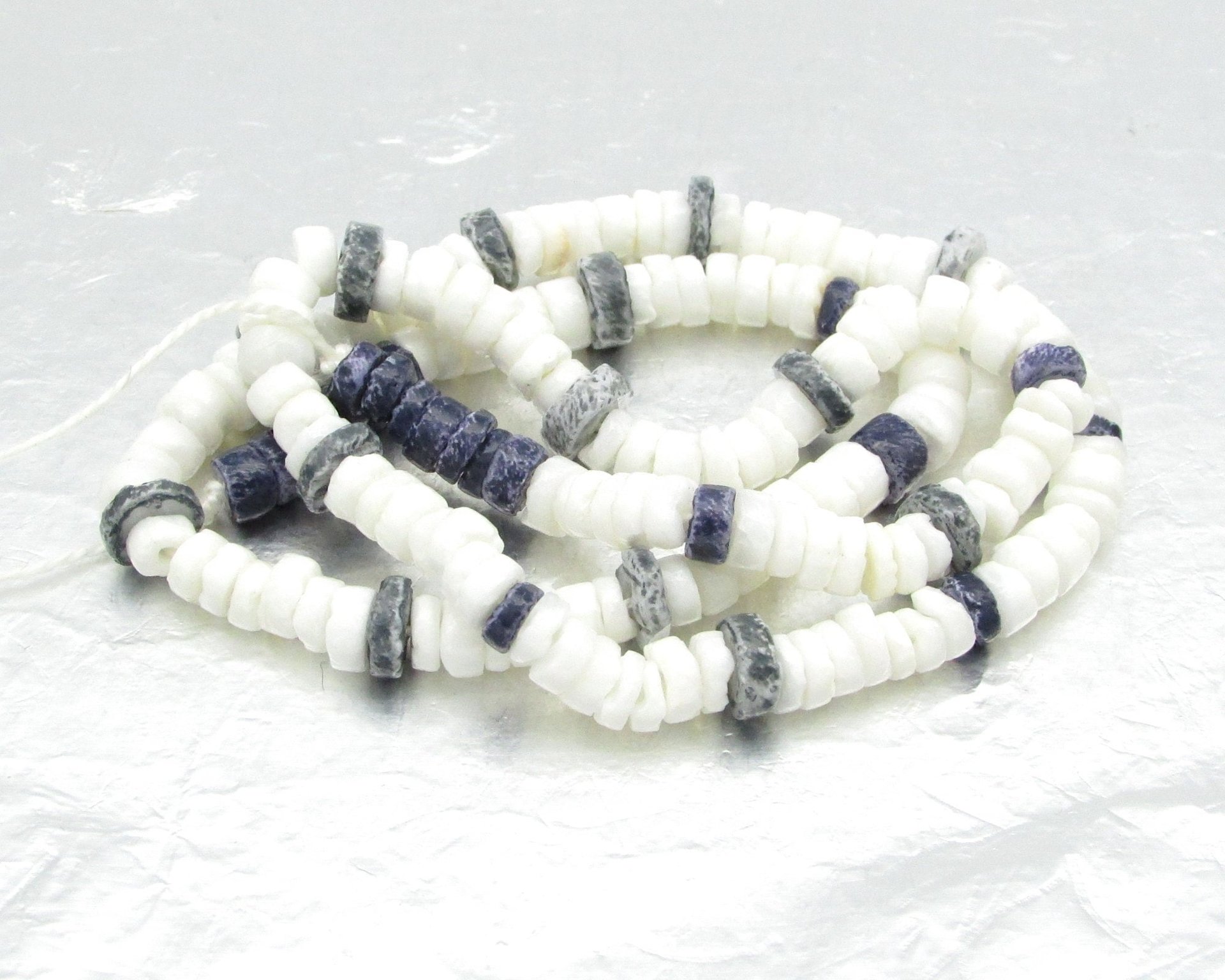15 inch strand of vintage heishi beads has 189 flat, round beads center-drilled with 1mm holes. The strand rustic, unfaceted rondelles has 35 dark blue and 154 opaque white glass beads. 