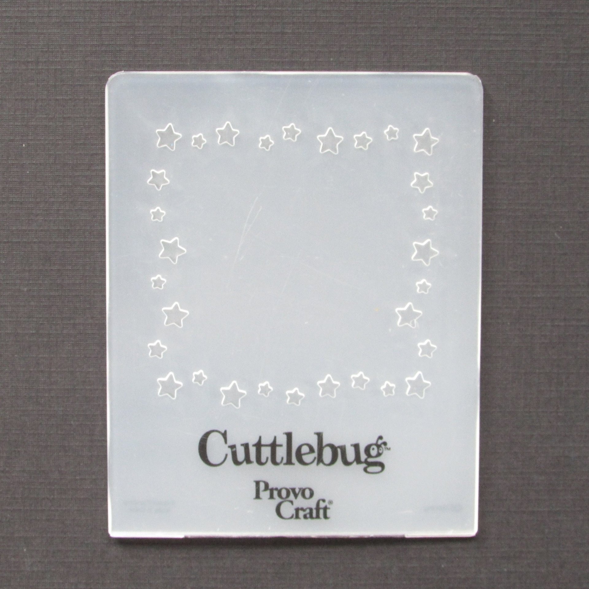 Cuttlebug embossing folder is flexible plastic with a whimsical star pattern for surrounding a square die-cut, photo, or text. Folder measures approximately 3.75 inches by 3 inches.