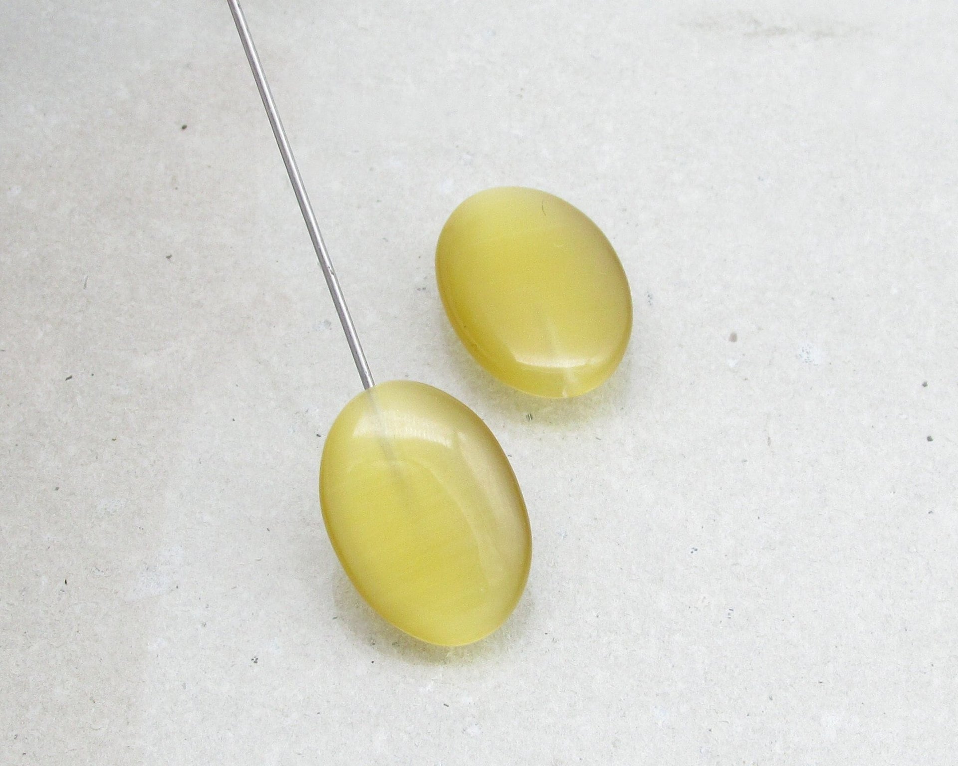 Half-drilled oval fiber optic glass pendant beads have a cat's eye effect when seen from different angles. Beads measure approximately 18mm long, 13mm wide, and 5-7mm thick.