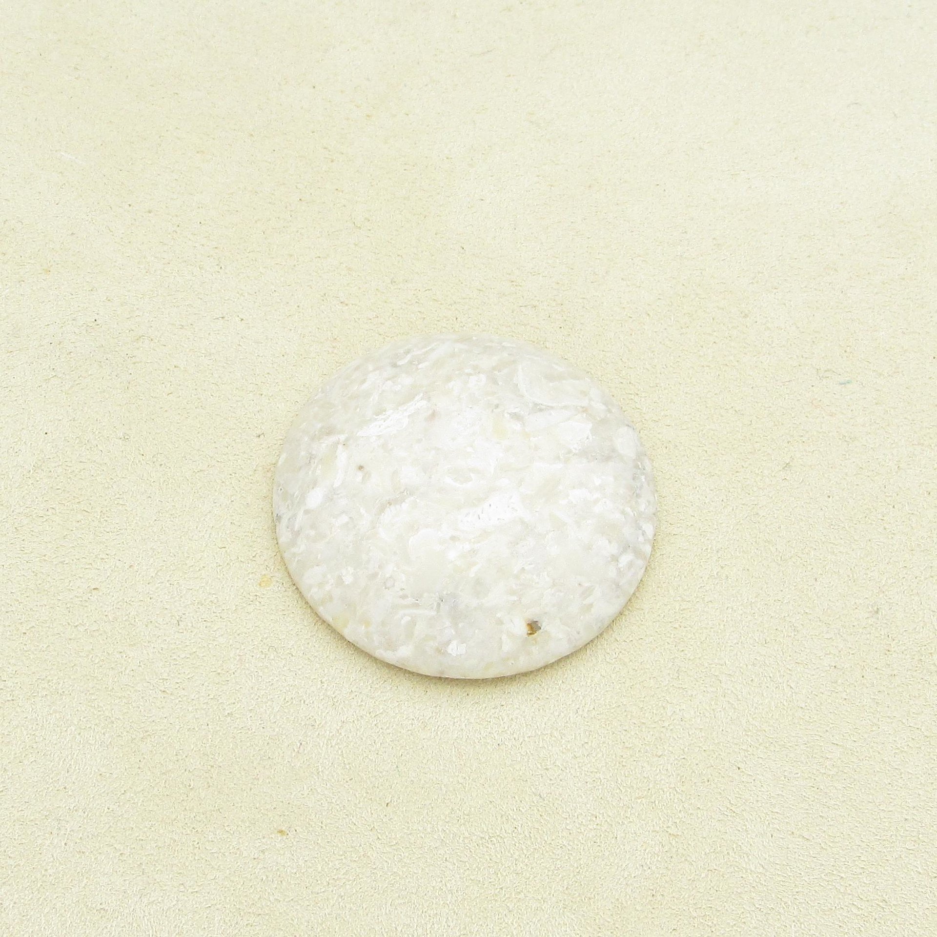 Opaque beige jasper cabochon is polished on both sides, with a domed top. Stone has mottled look, with lighter patches of cream and some small translucent areas. Low dome cabochon measures approximately 30mm across and 6mm thick at the center. 