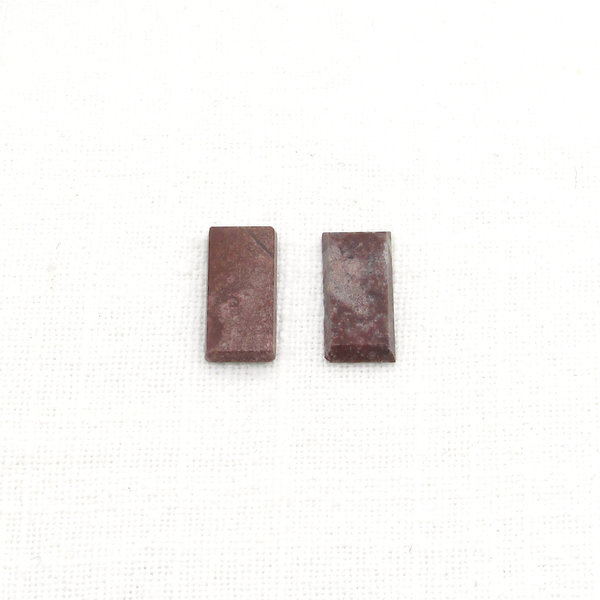 Dark red jasper cabochons are flat rectangles measuring approximately 16.3x8mm and 2.3.mm thick with beveled sides. Each opaque, polished stone is unique with inclusions forming patches and/or veins of beige, gray, and black.  Lighter-colored areas have more translucency than the rest of the stone.