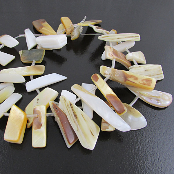 Graduated mother of pearl strand has 36 flat spike beads. Top-drilled irregularly shaped beads range from 10mm to 20mm long and 3mm. Beads are hand cut irregular shapes. One side is iridescent off-white nacre. The reverse side is polished, but retains the natural striated light brown color of the outer shell.