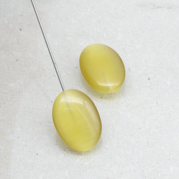 Half-drilled oval fiber optic glass pendant beads have a cat's eye effect when seen from different angles. Beads measure approximately 18mm long, 13mm wide, and 5-7mm thick.